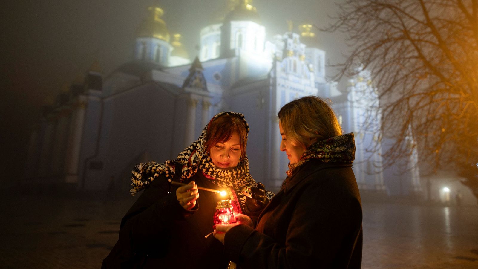 Mujeres encienden una vela en un ambiente invernal y brumoso, frente a una catedral.  La llama representa esperanza.