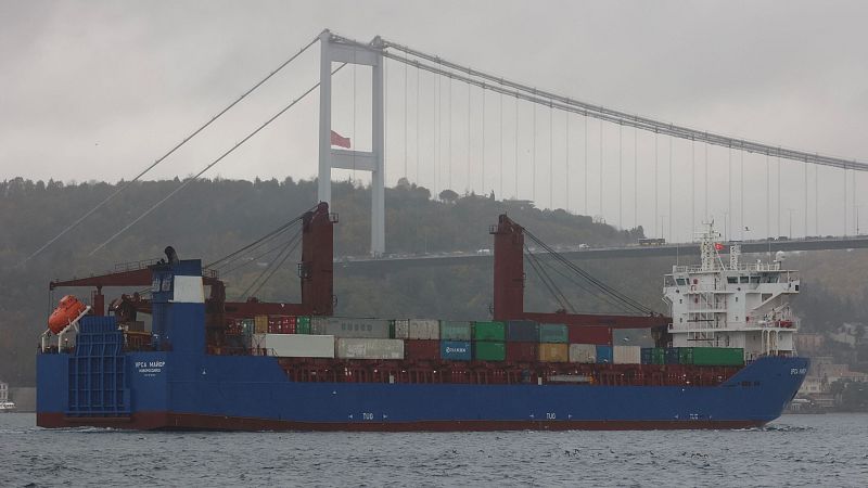 Carguero Ursa Major navegando, casco azul oscuro y blanco, transportando contenedores. Cielo nublado.