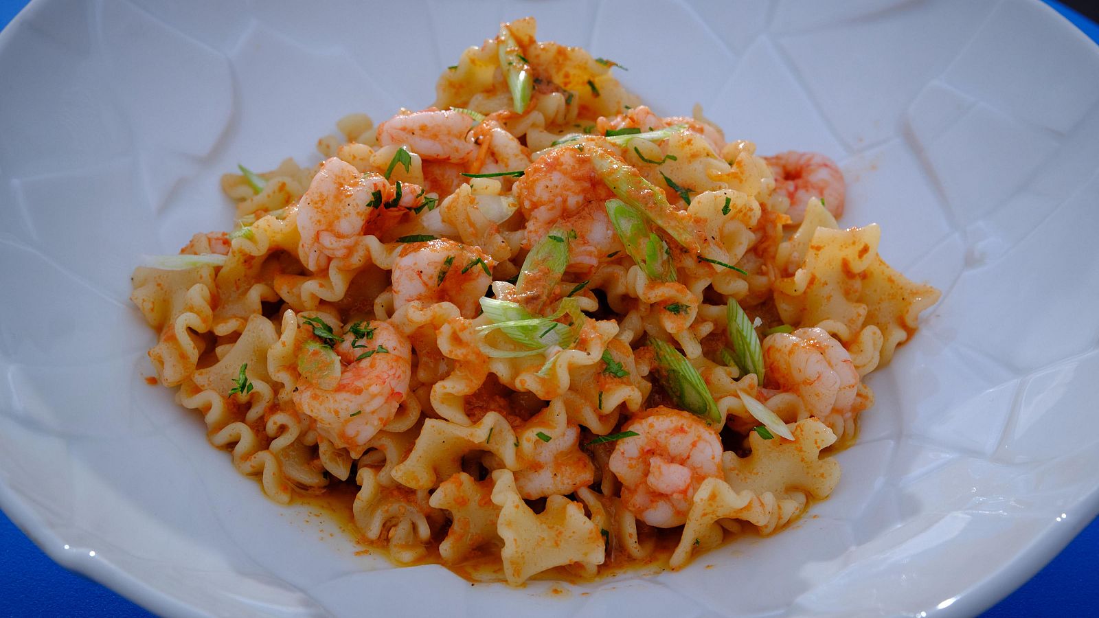 Pasta con gambas al ajillo en un plato blanco con forma floral; pimentón rojo y cebollino fresco como decoración.