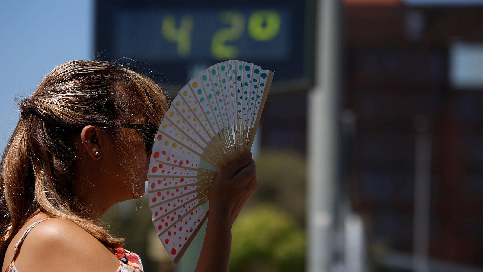 Una mujer se abanica junto a un termómetro de calle que marca 42 grados en Córdoba