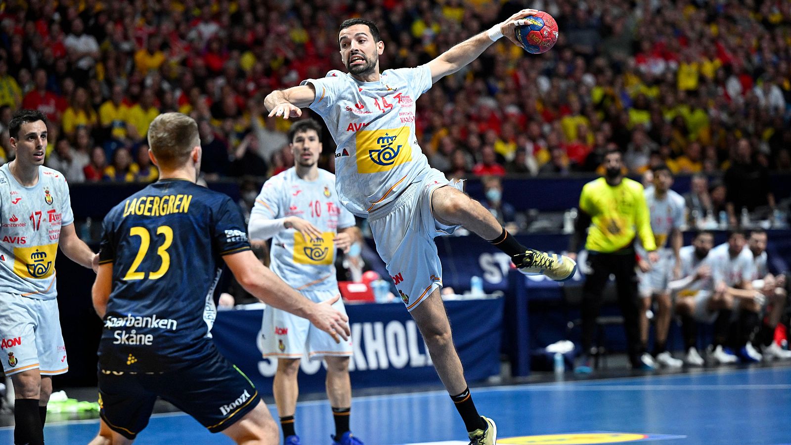 Partido de balonmano: jugador #14 (camiseta clara con logotipos) salta para lanzar.  Otro jugador (#23, camiseta oscura) y dos compañeros (#17, #10, camisetas claras) visibles.