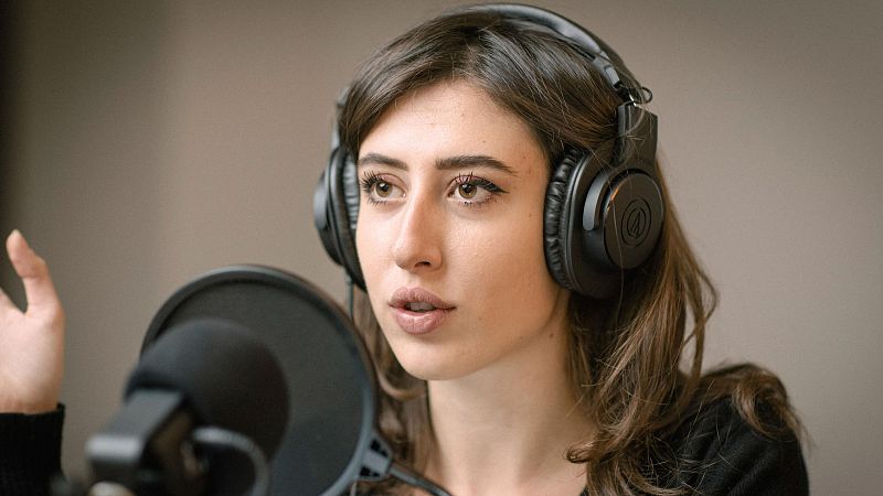 Periodista con auriculares y micrófono, hablando con expresión seria y gestos enfáticos.  Posible grabación de un informe.