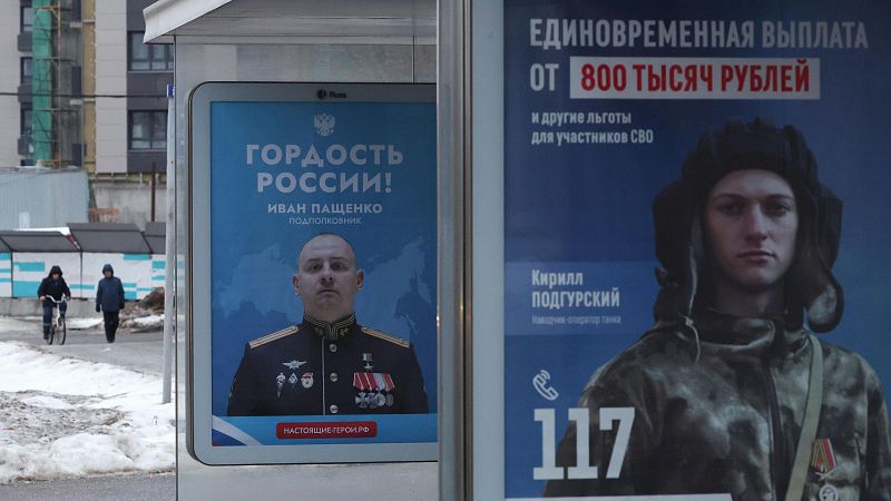Vallas publicitarias en Moscú muestran a militares rusos, condecoraciones y beneficios económicos para unirse a la operación militar. Se observa nieve en el suelo.