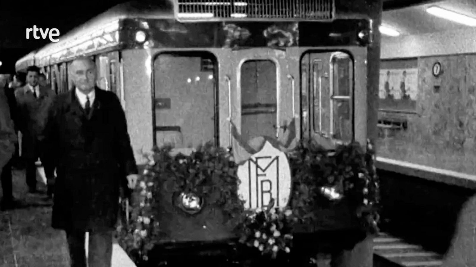 Celebración del centenario del metro de Barcelona: vagón decorado, hombre en traje y otros asistentes en el andén.