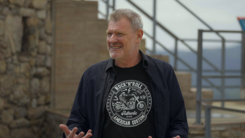 Jaume Vilalta, con camisa negra sobre camiseta con diseño rockero, gesticula en exterior rocoso. Sonríe.