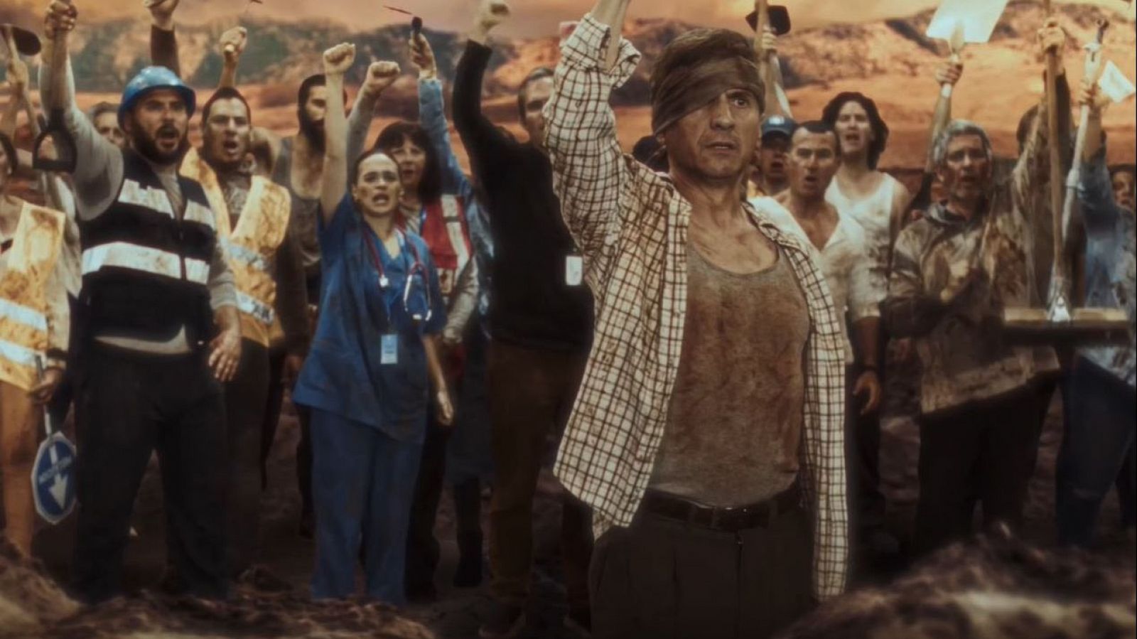 José Mota, vendado y con ropa manchada, en medio de una multitud que protesta en un paisaje desolado tras una posible catástrofe natural.  Especial Nochevieja.