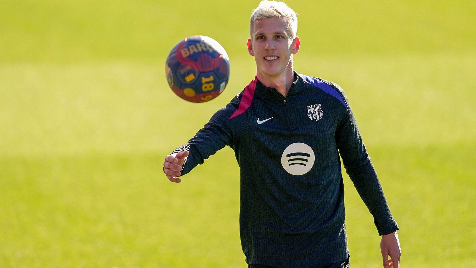 Jugador del FC Barcelona en entrenamiento, con equipación azul oscuro y balón en mano. Fondo de césped.