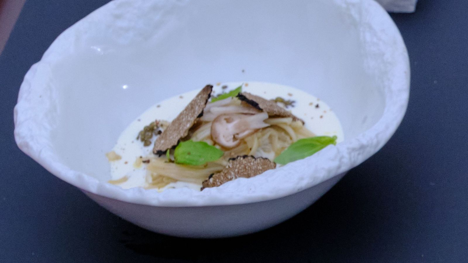 Pasta cremosa con setas enoki, trufa negra y albahaca en bol blanco.  Presentación cuidada, posiblemente de un programa de cocina.