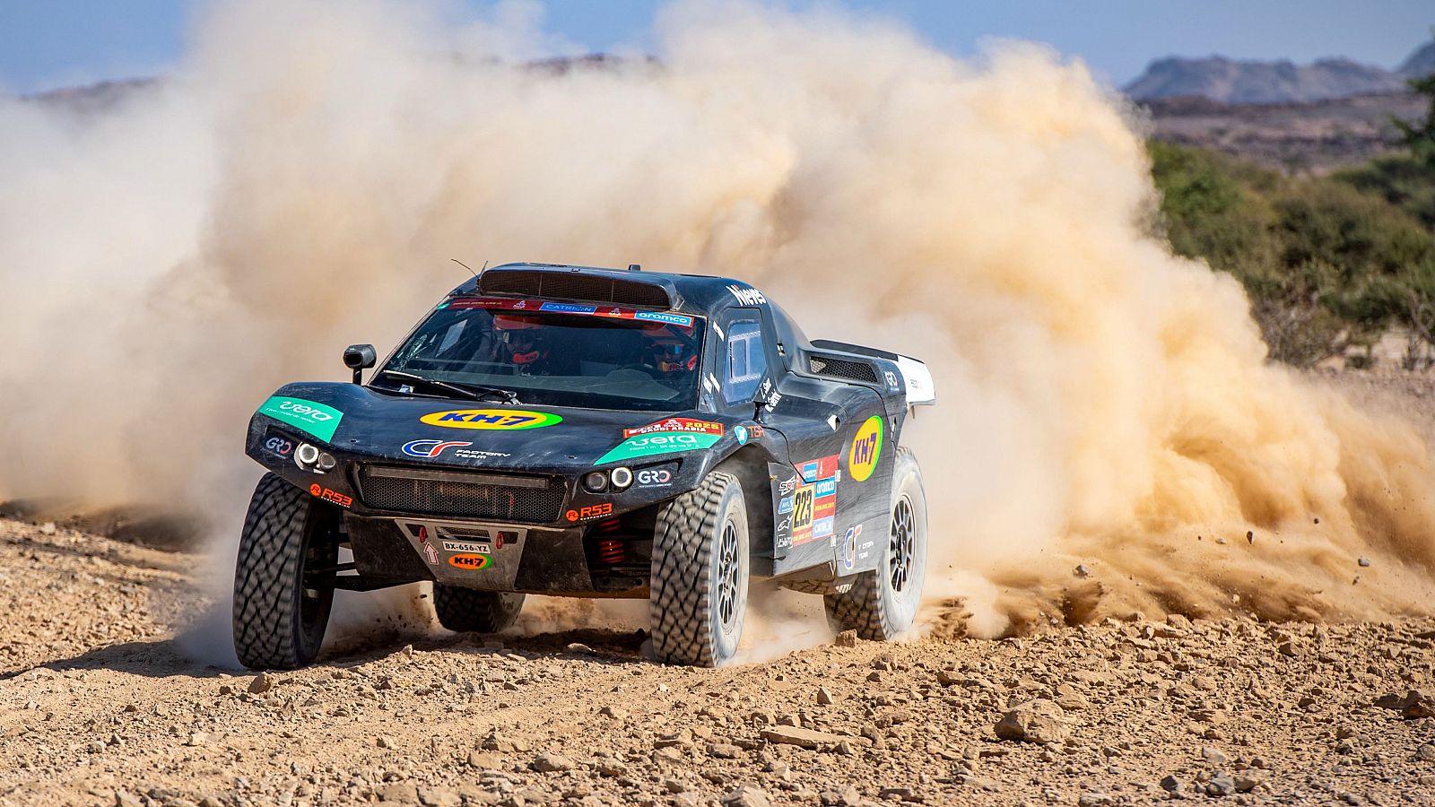 Buggy de carreras (nº 228) en el Rally Dakar 2025, levantando polvo en un terreno árido.  Se ven los patrocinadores KH7, GO y Cero.
