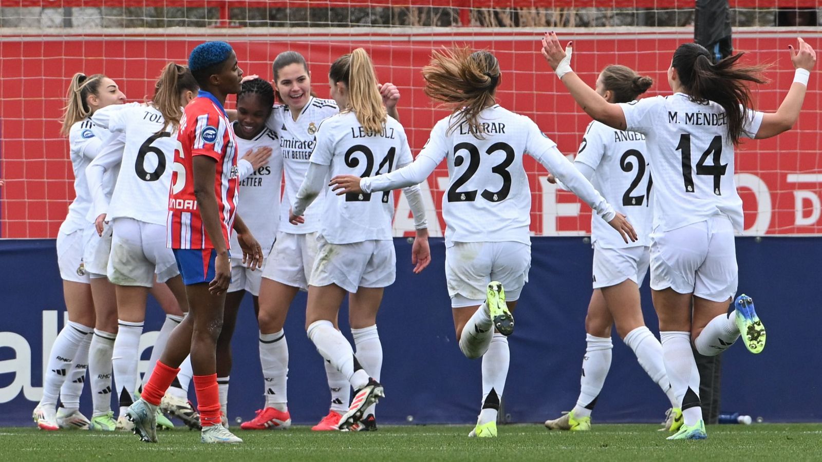 Celebración de jugadoras del Real Madrid tras un gol, con dorsales visibles (6, 24, 23, 2, 14) y nombres como Toledo, Leomulz, Larrar, Angel y M. Mendez.  Jugadoras del Atlético de Madrid aparecen con semblante serio en segundo plano.