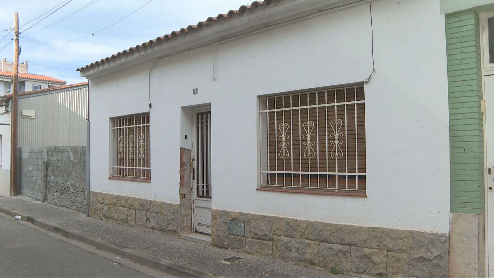 Casa blanca de una planta con zócalo de piedra, ventanas con rejas y puerta blanca con cristales.  Número 8 visible.