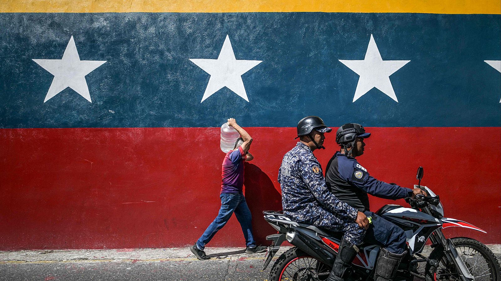 Un hombre camina frente a un mural con la bandera venezolana mientras dos agentes de la Policía Nacional Bolivariana pasan a su lado en Caracas, el 8 de enero de 2025.