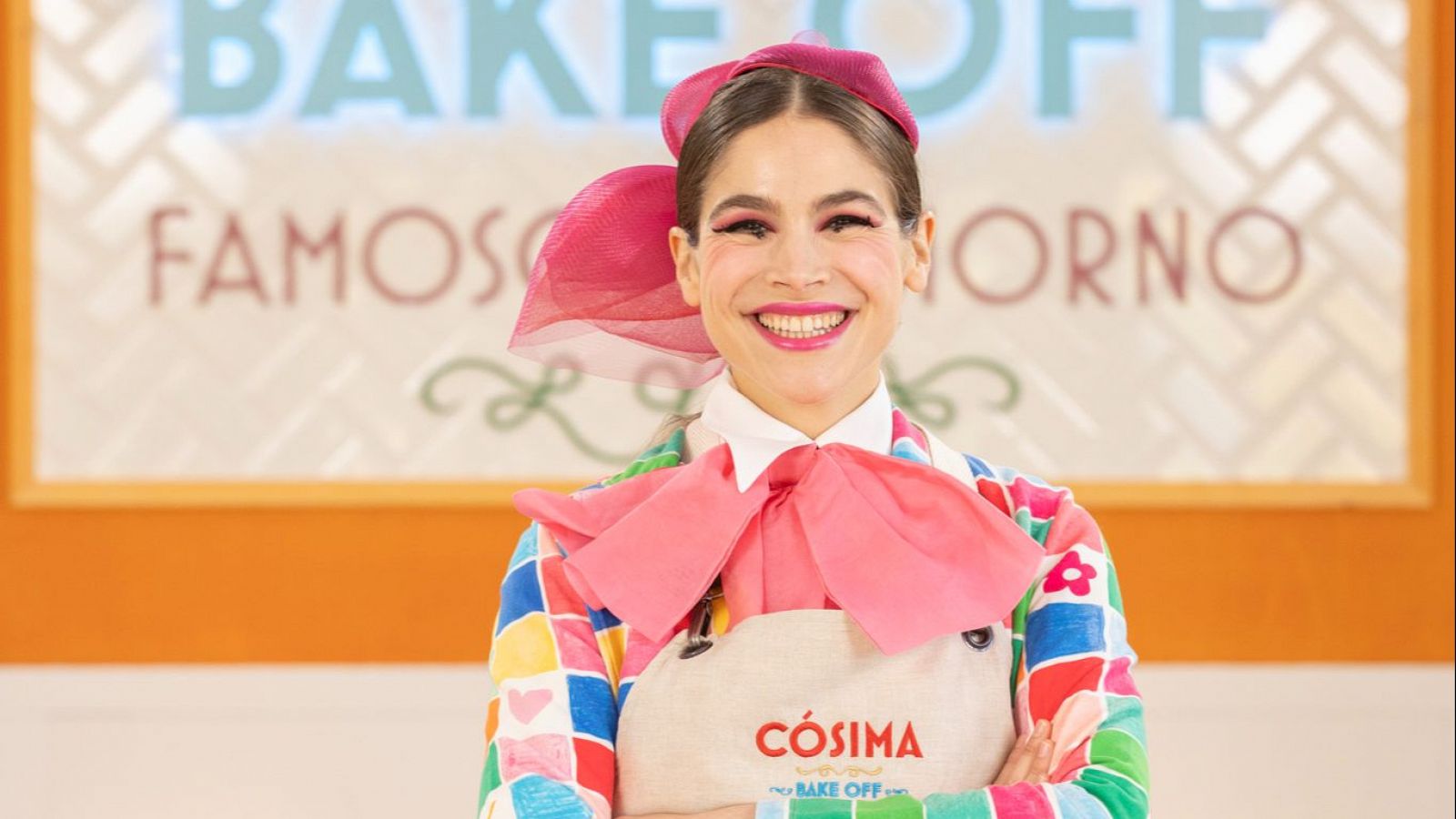 Cósima Ramírez, con camisa multicolor, lazo rosa y tocado, sonríe a cámara en el set de 'Bake Off: Famosos al horno'.