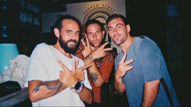 Imagen de tres hombres jóvenes en ambiente festivo, con un cartel de "SACRED PLACE" al fondo y la frase "Justicia para Diego".