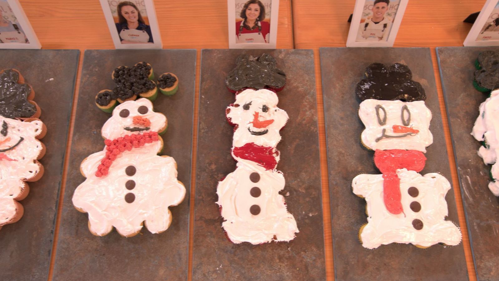 Cuatro muñecos de nieve comestibles, con sombreros y bufandas de colores, sobre tablas individuales.  Merengue y magdalenas como ingredientes principales.