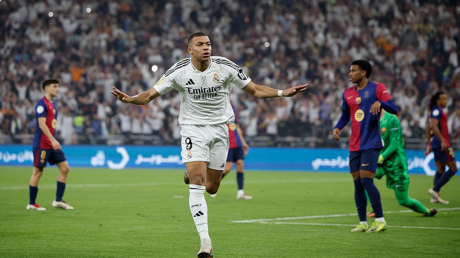 Celebración de gol de un jugador con la camiseta del Real Madrid, número 9 y patrocinador Emirates. Estadio lleno de público y jugadores contrarios al fondo.