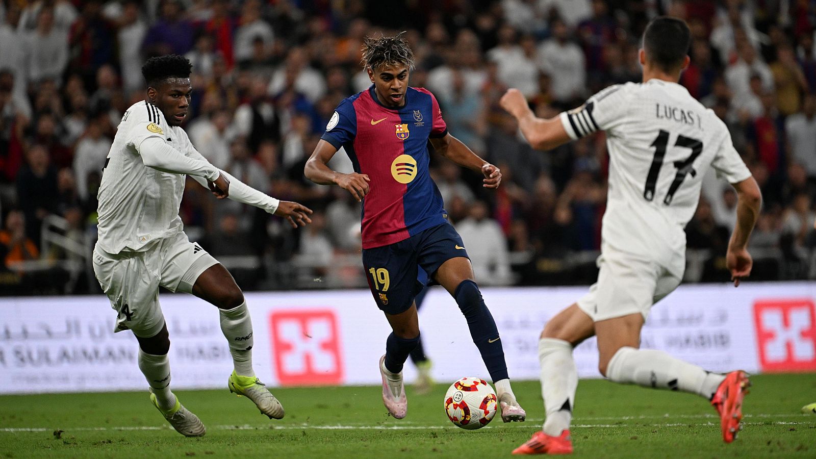 Lamine Yamal (Barcelona, dorsal 19) conduce el balón entre Tchouameni y Lucas Vázquez (Real Madrid)