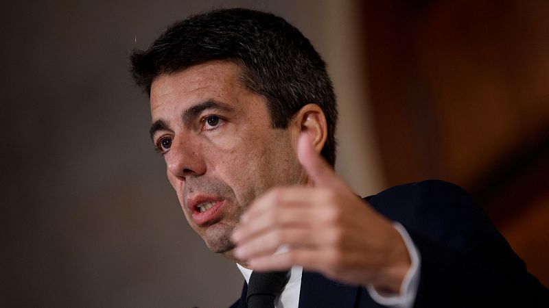 Imagen de Ximo Puig hablando, probablemente en una rueda de prensa. Expresión seria, traje oscuro y corbata. Gesto con la mano derecha.