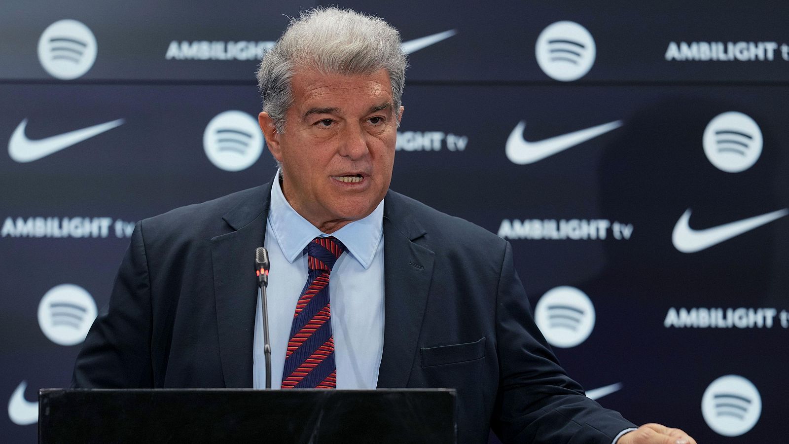 Rueda de prensa de Joan Laporta, presidente del FC Barcelona, con traje oscuro y corbata a rayas. Fondo con logos de patrocinadores.