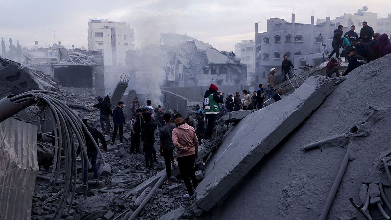 Escombros y personas entre los restos de un edificio destruido.  Un trabajador humanitario con chaleco distintivo participa en las tareas de rescate.