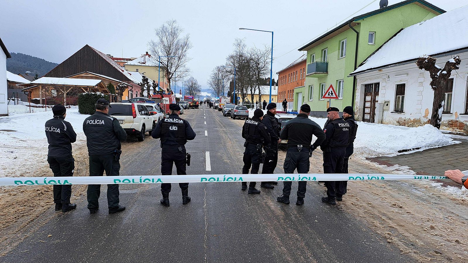 Policías eslovacos en una calle nevada acordonada tras un incidente grave. Uniformes oscuros con "POLICIA" en la espalda.  Posible escena del crimen.