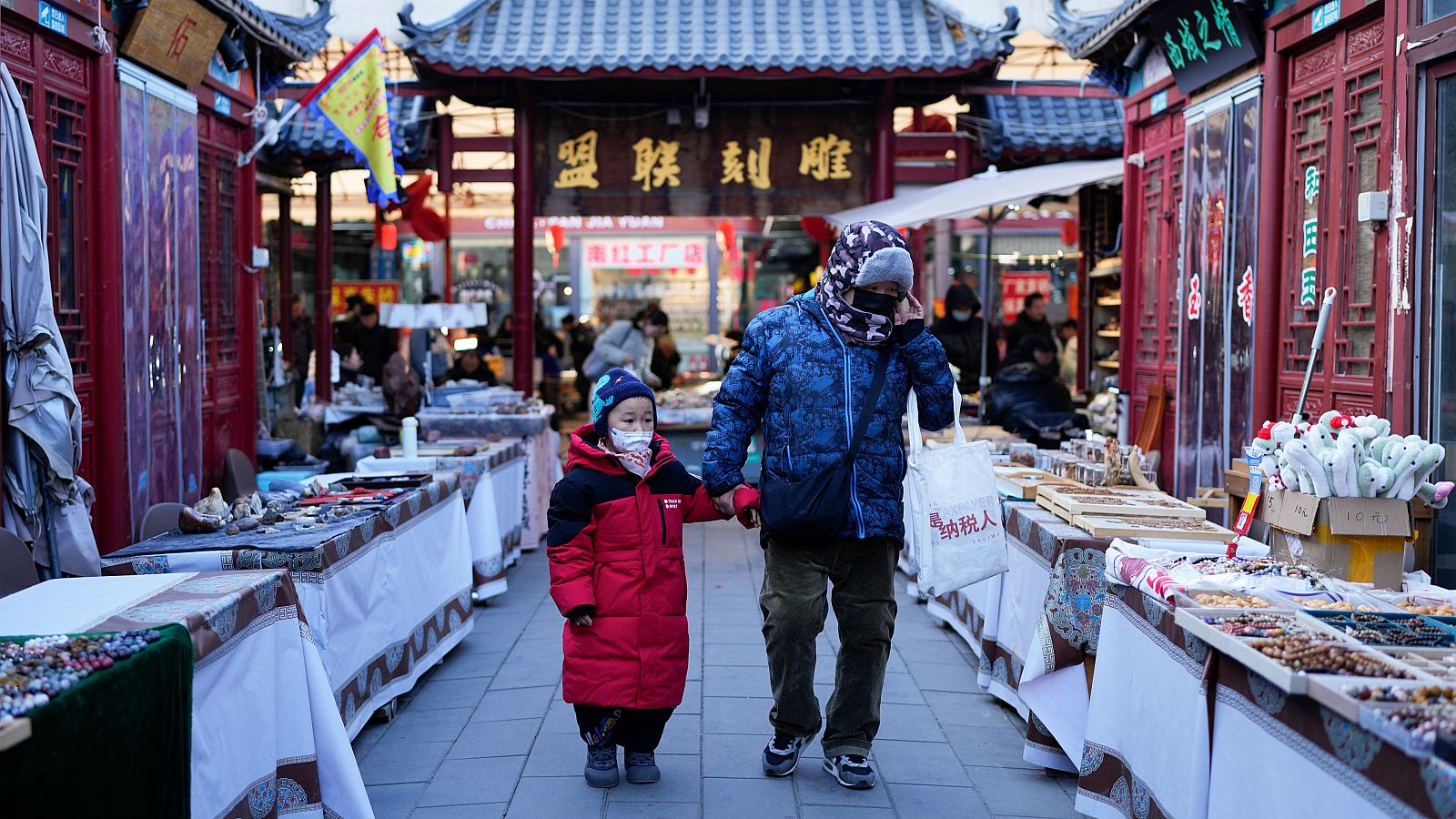 Un niño y un adulto caminan de la mano en un mercado de Pekín, China