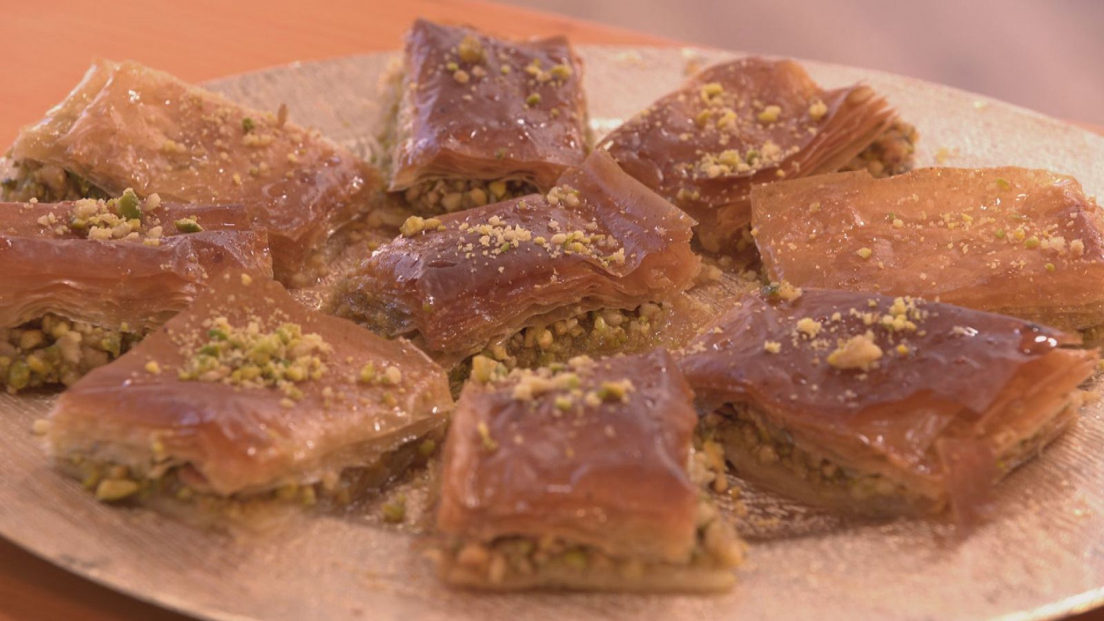 Baklava con capas de masa filo crujiente, pistachos y miel, servido en un plato brillante.