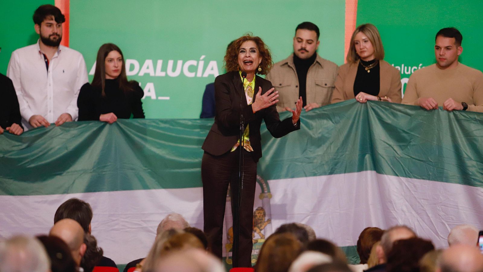 Discurso de María Jesús Montero en un acto político del PSOE andaluz.  Se aprecia una bandera andaluza y un atril con micrófono.