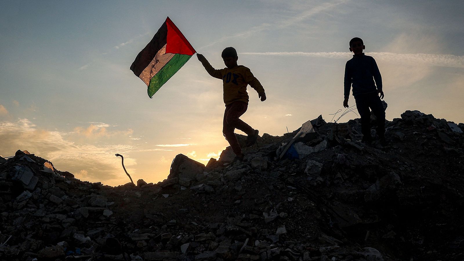 Un niño corre con una bandera palestina sobre una montaña de escombros en un campo de desplazados en el centro de Gaza