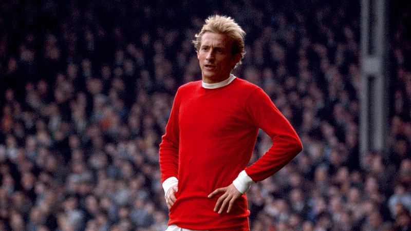 Denis Law, futbolista del Manchester United, en un campo de fútbol con público.  Imagen en la que se anuncia su muerte a los 84 años.
