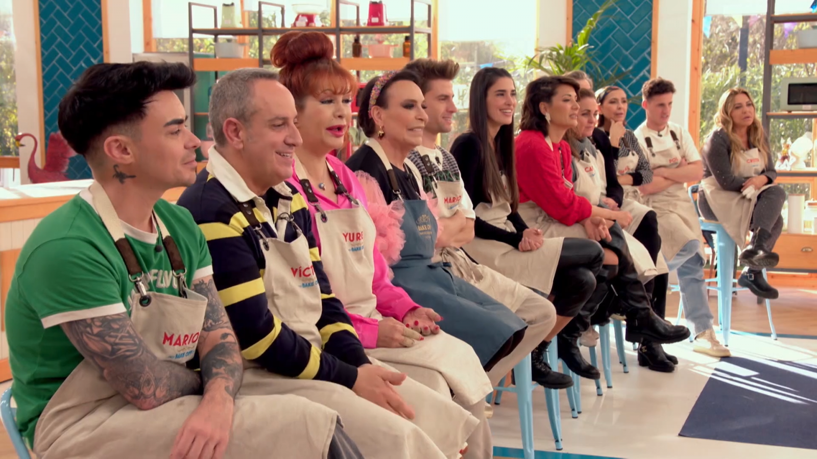 Cata a ciegas en 'Bake Off: famosos al horno'. Concursantes con delantales beige y nombres visibles, sentados en taburetes azules, muestran diversas expresiones faciales.