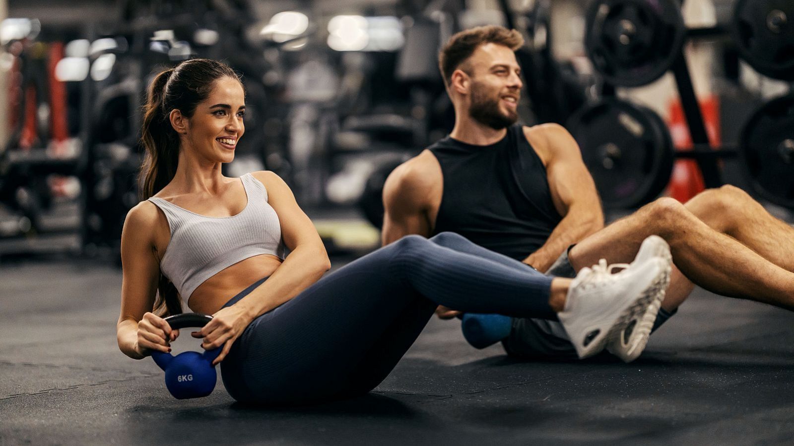 Una chica y un chico haciendo abdominales laterales con una pesa de 6 Kg en el gimnasio