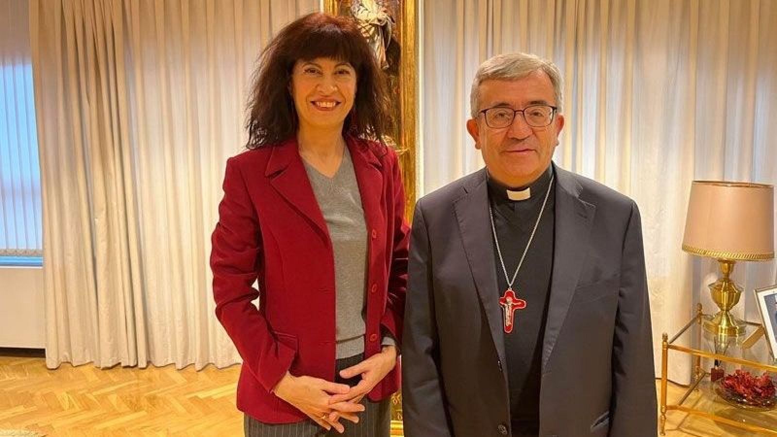 Encuentro entre la Ministra de Igualdad y el presidente de la Conferencia Episcopal Española. Ambos posan sonrientes, ella con chaqueta roja y él con traje oscuro.