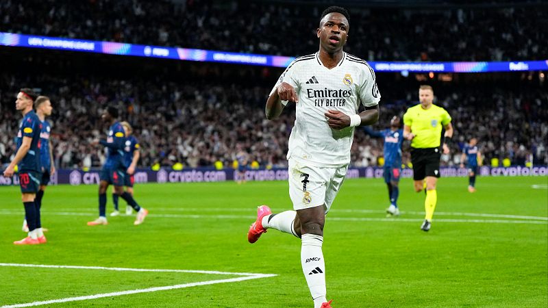 Celebración de gol de Vinicius Jr. con la camiseta del Real Madrid; botas rosas; fondo con jugadores rivales y árbitro.