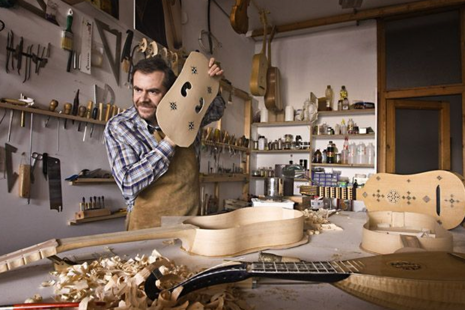 Artesano construyendo instrumentos de cuerda con métodos tradicionales.  Se observa una tapa armónica con dos agujeros en forma de 'C' y detalles decorativos.