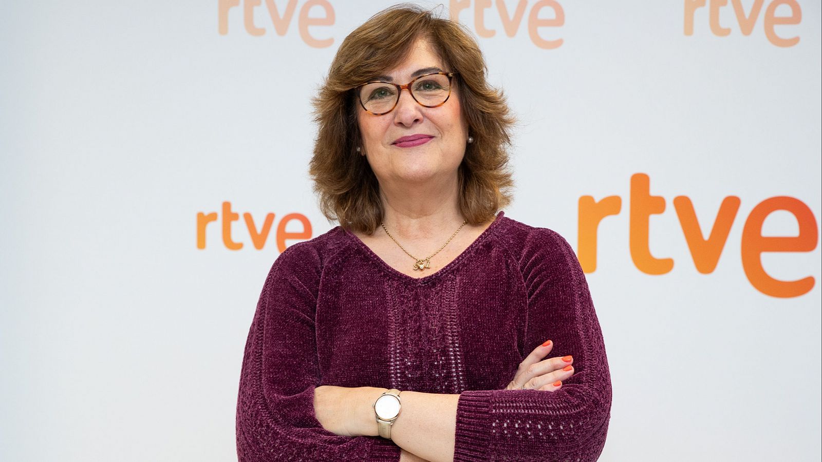 Ana Cerrada, de Comunicación RTVE, en foto corporativa: jersey granate, gafas, brazos cruzados, fondo con logo RTVE.
