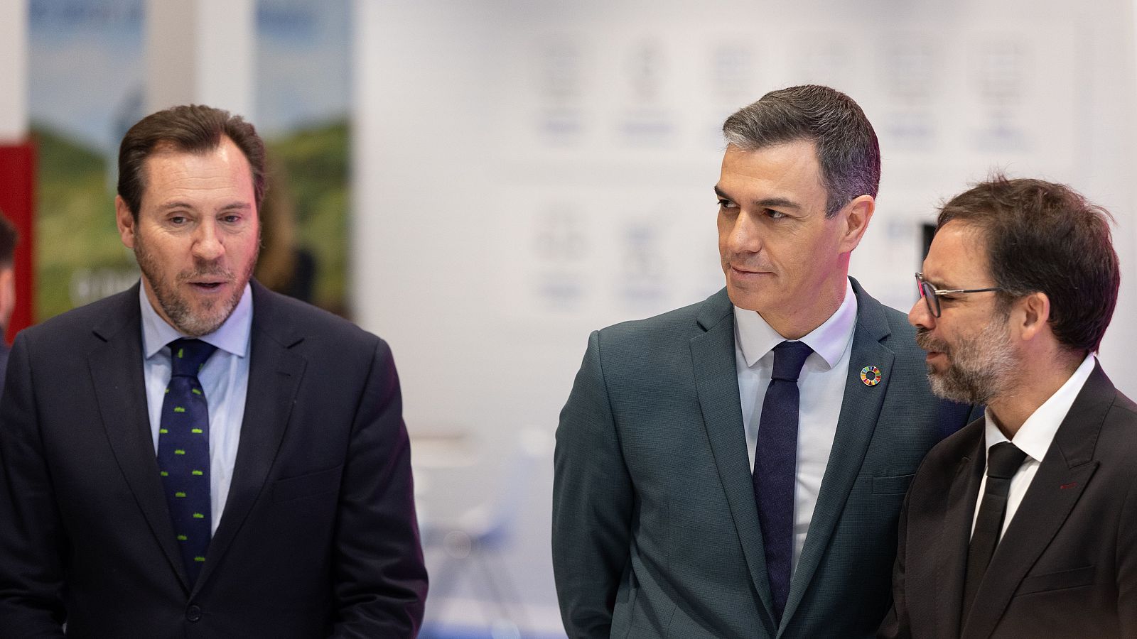 El presidente español, Pedro Sánchez, y dos hombres en traje oscuro, con corbatas de distintos colores, participan en un evento oficial.  Sus expresiones son serias.