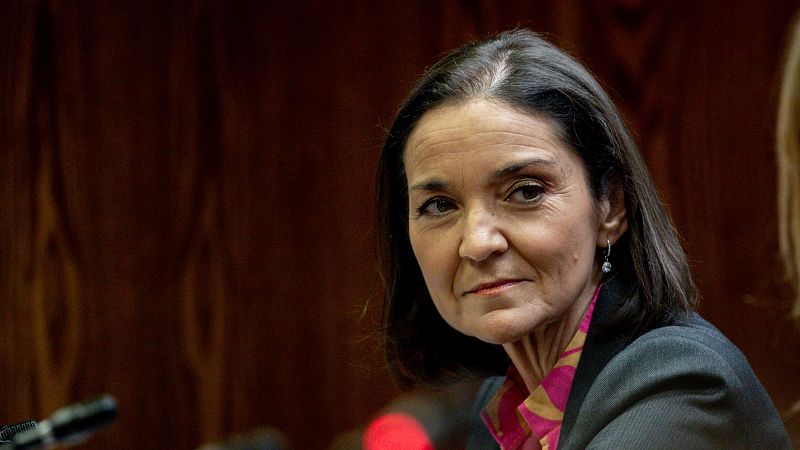 Imagen de Reyes Maroto con blusa rosa y chaqueta oscura, expresión seria, en lo que parece una rueda de prensa con micrófonos visibles.