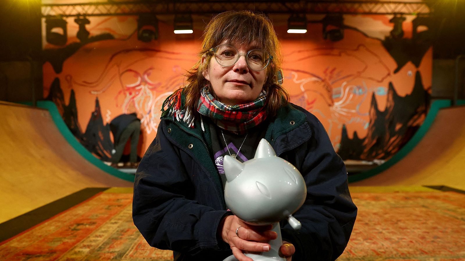 Anouk Ricard, con gafas y chaqueta azul marino, sostiene una figura de gato en un espacio con grafitis y una rampa. Fotografía de Romain Perrocheau/AFP.