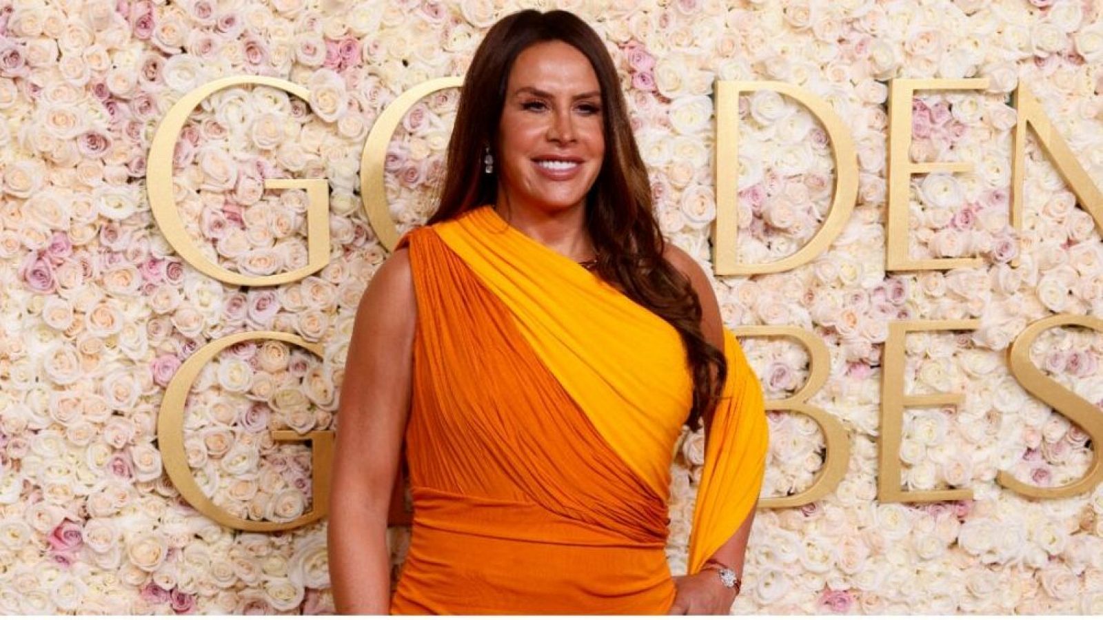 Actriz con vestido naranja degradado y un solo tirante en una ceremonia con fondo floral y letras doradas que dicen "GOLDEN GLOBES".