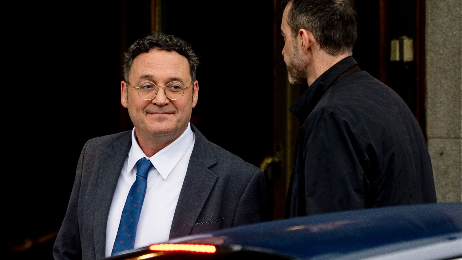 Álvaro García Ortiz, fiscal general del Estado, sale del Tribunal Supremo con una leve sonrisa; viste traje oscuro, gafas y corbata azul con lunares blancos.