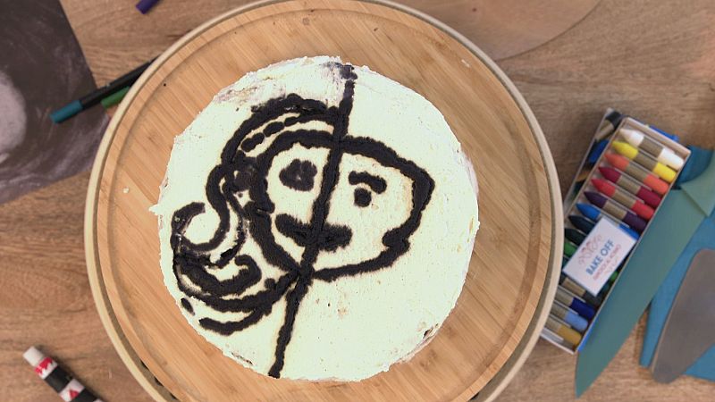 Autorretrato en crema de chocolate sobre una tarta redonda, junto a utensilios de decoración y lápices comestibles Bake Off.