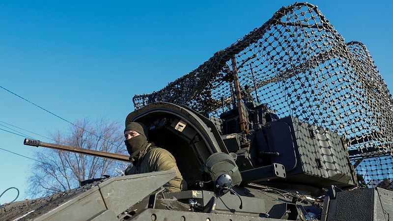 Soldado en vehículo militar camuflado, alerta y mirando a la izquierda.  Invierno, posible zona de conflicto cerca de una aldea.
