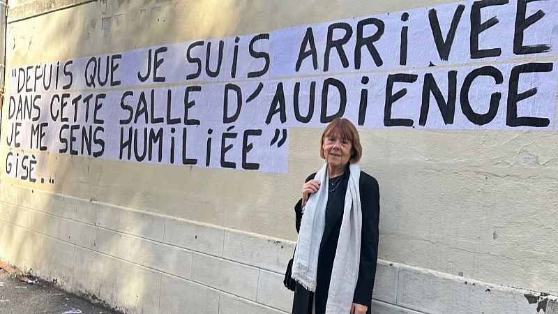 Mujer con abrigo negro y bufanda clara posa junto a un muro con una frase escrita en francés: "Desde que llegué a esta sala de audiencias me siento humillada".