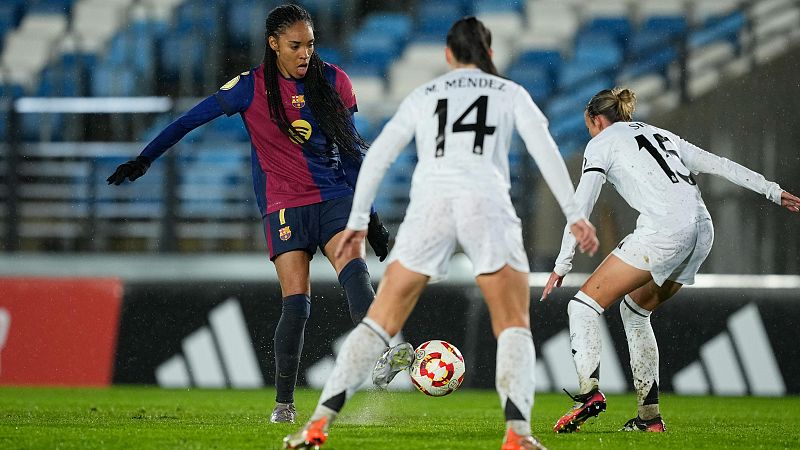 Jugadora del Barça a punto de chutar, marcada por dos rivales con dorsales 14 y 15, en un campo mojado.  Tensión máxima.