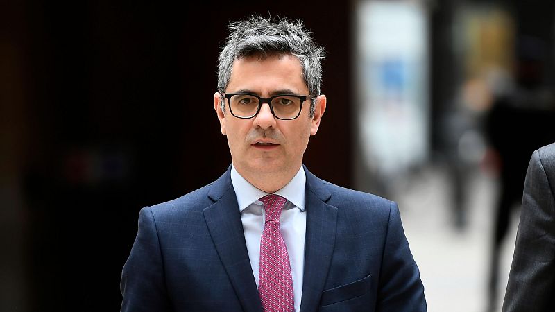 Félix Bolaños, ministro español, en retrato con traje azul marino, camisa blanca y corbata rosa con puntos. Fondo público desenfocado.