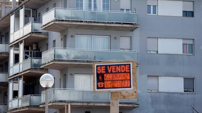 Edificio de apartamentos en venta. Fachada gris, balcones con cristales y aire acondicionado visible. Cartel "SE VENDE" con números de teléfono.