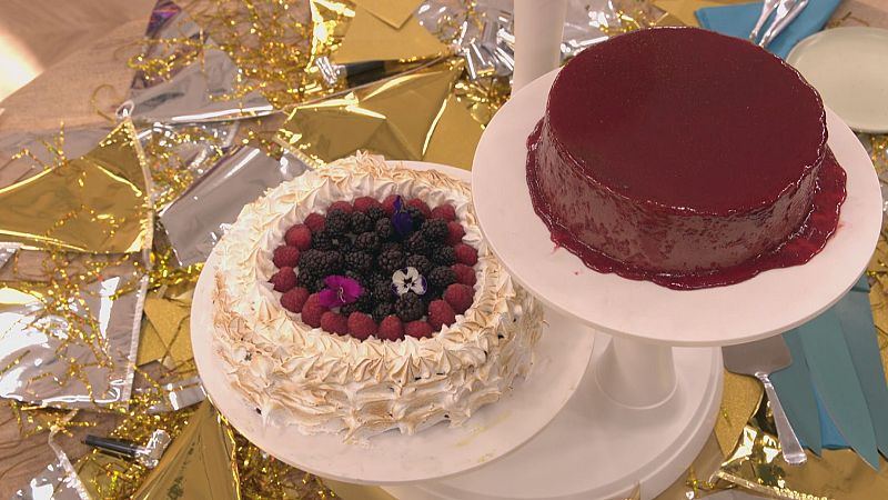Dos tartas decoradas, una con glaseado rojo brillante y otra con merengue y frutos rojos, sobre soportes blancos, rodeadas de confeti dorado y plateado.