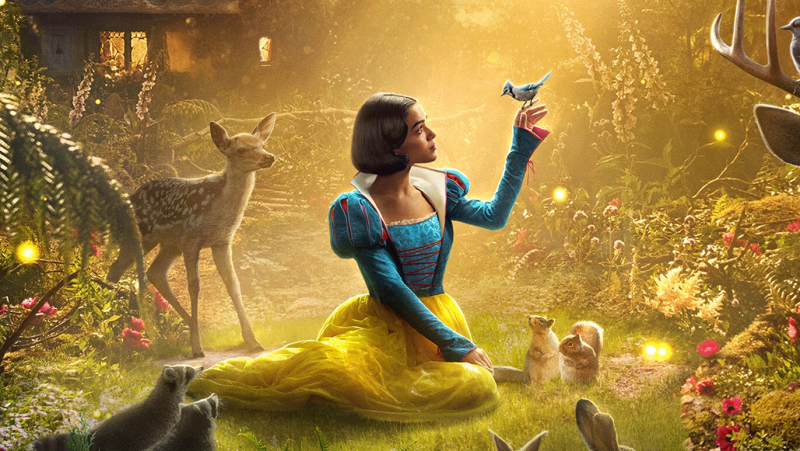 Blancanieves, interpretada por Rachel Zegler, en un bosque con animales, viste un vestido amarillo y azul.  Un pájaro azul descansa en su mano.