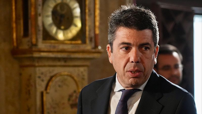 El presidente de la Generalitat Valenciana, en Les Corts, viste traje oscuro y corbata con puntos, con expresión seria mientras habla.